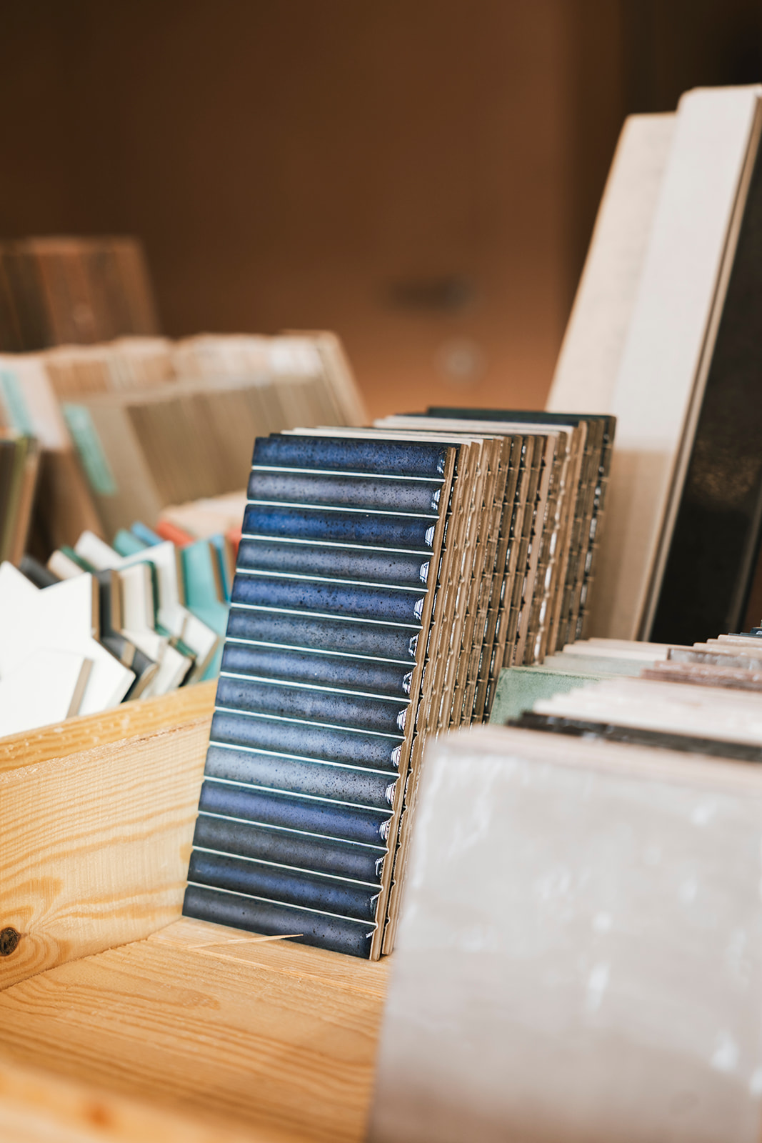 Diverse keramische wandtegels en vloertegels in verschillende kleuren en texturen in houten rekken bij tegelwinkel Oblon in Roeselare